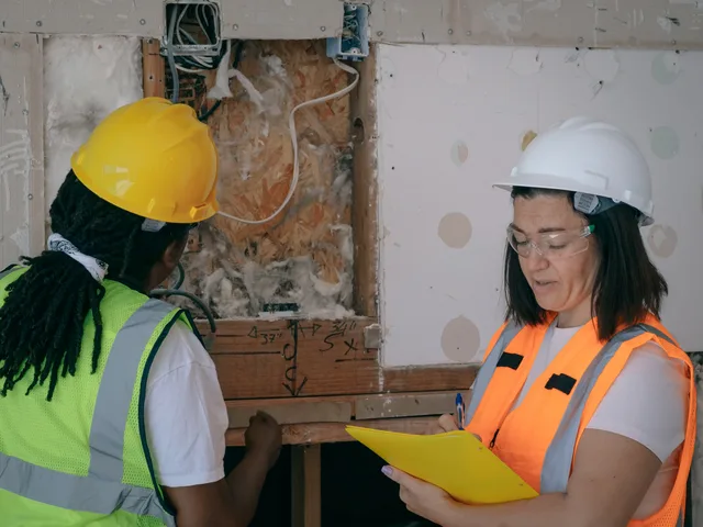 Two workers in protective gear inspecting and taking notes during a construction site electrical inspection. ID06: vad krävs av företag och arbetare?