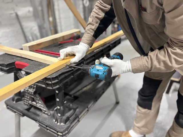 A carpenter using a power drill to work on wooden planks in an indoor workshop setting. Referenser från hantverkare: så kontrollerar du dem